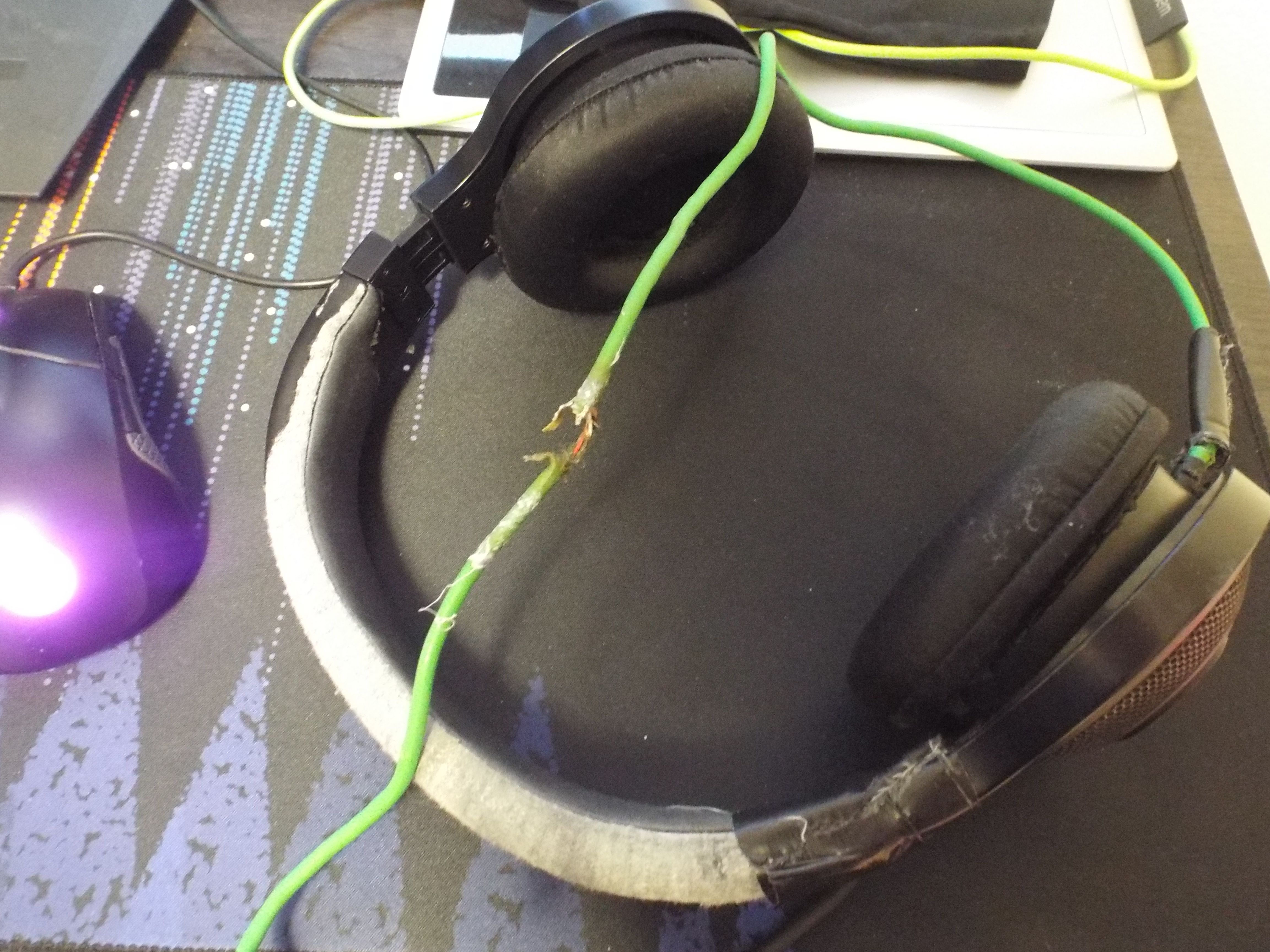 a photograph of a decade old razer kraken headset. the cable is clearly broken in the center of the frame. a section of the cable near where it connects to the headset has duct tape wrapped around it, as does part of the headset band. the majority of the covering on the headset band and earmuffs have long since worn off.